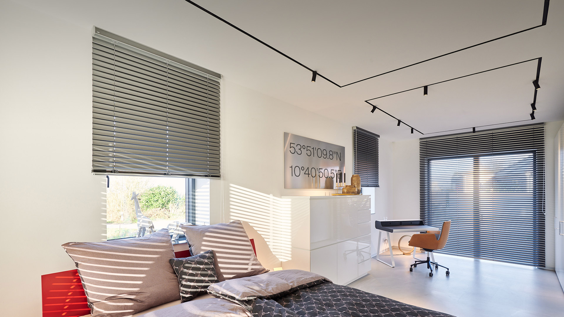Camera da letto e area lavoro moderna con sistema di binari magnetici Artemide Vector Magnetic a soffitto, veneziane che filtrano la luce naturale