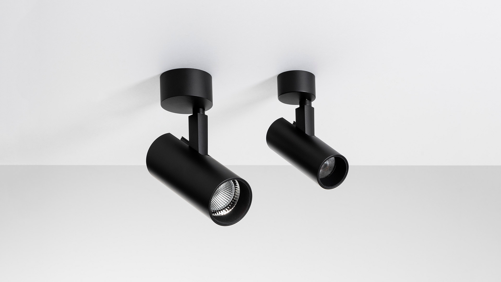 Two black Artemide Vector Ceiling adjustable spotlights mounted on white ceiling, cylindrical body with directional arm
