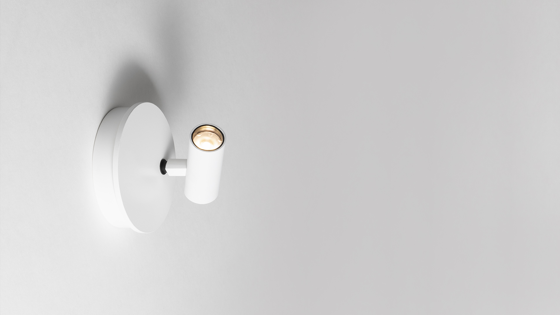 Artemide Vector Wall spotlight in white, featuring an adjustable cylindrical head mounted on a circular wall base, emitting warm focused light.
