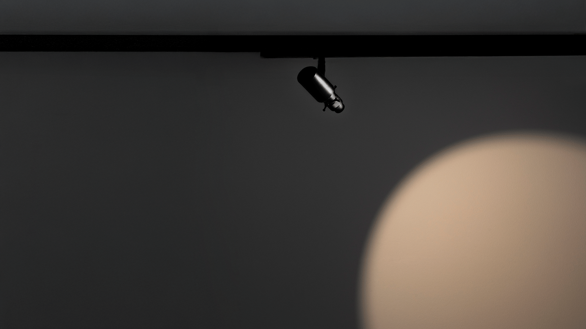 Artemide Vector track spotlight in black, mounted on a ceiling rail, directing focused light onto a wall surface below.