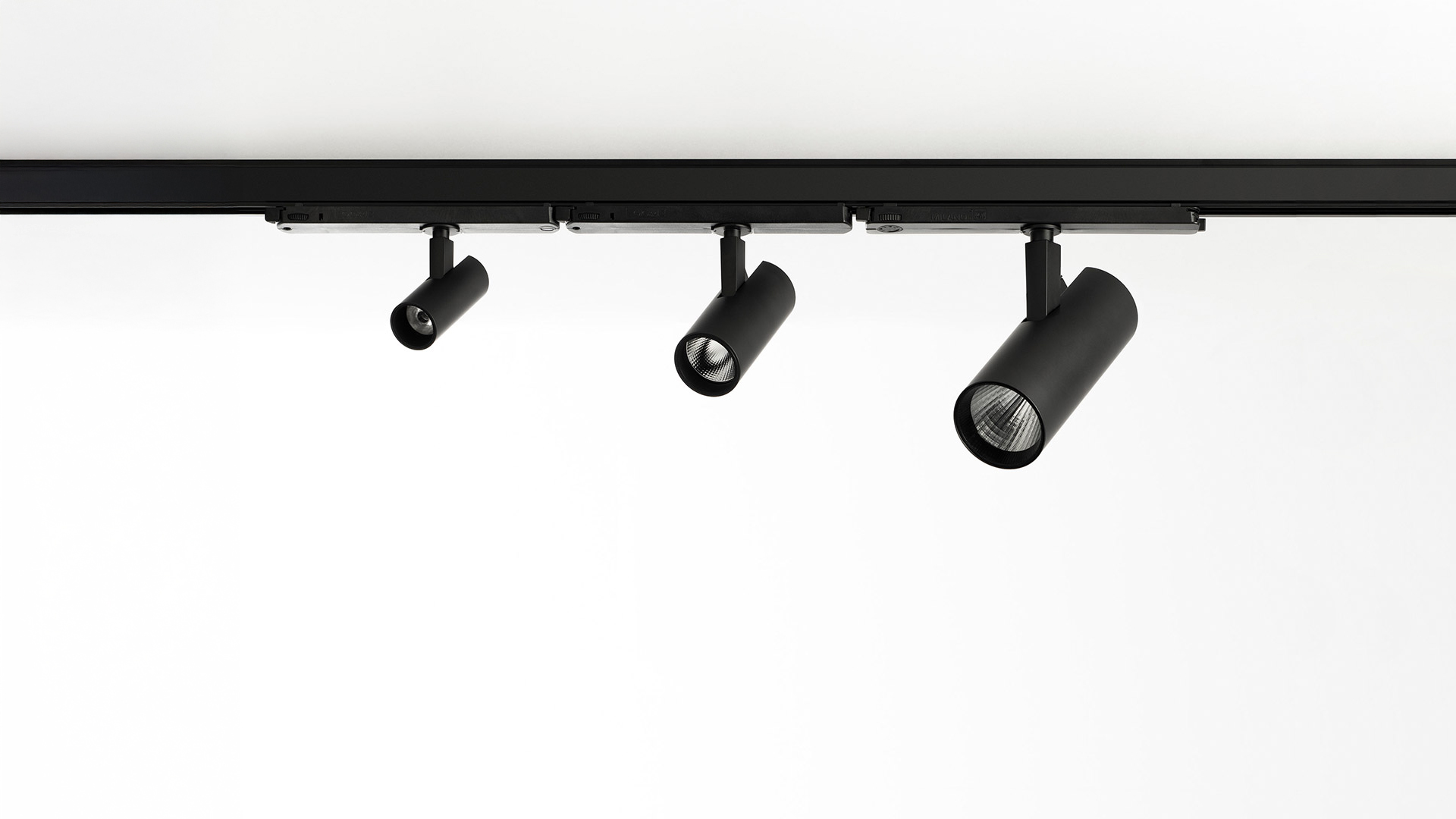 Faretto cilindrico nero Artemide Vector Track 230V montato su binario a soffitto, proietta un fascio di luce viola vivido sulla parete