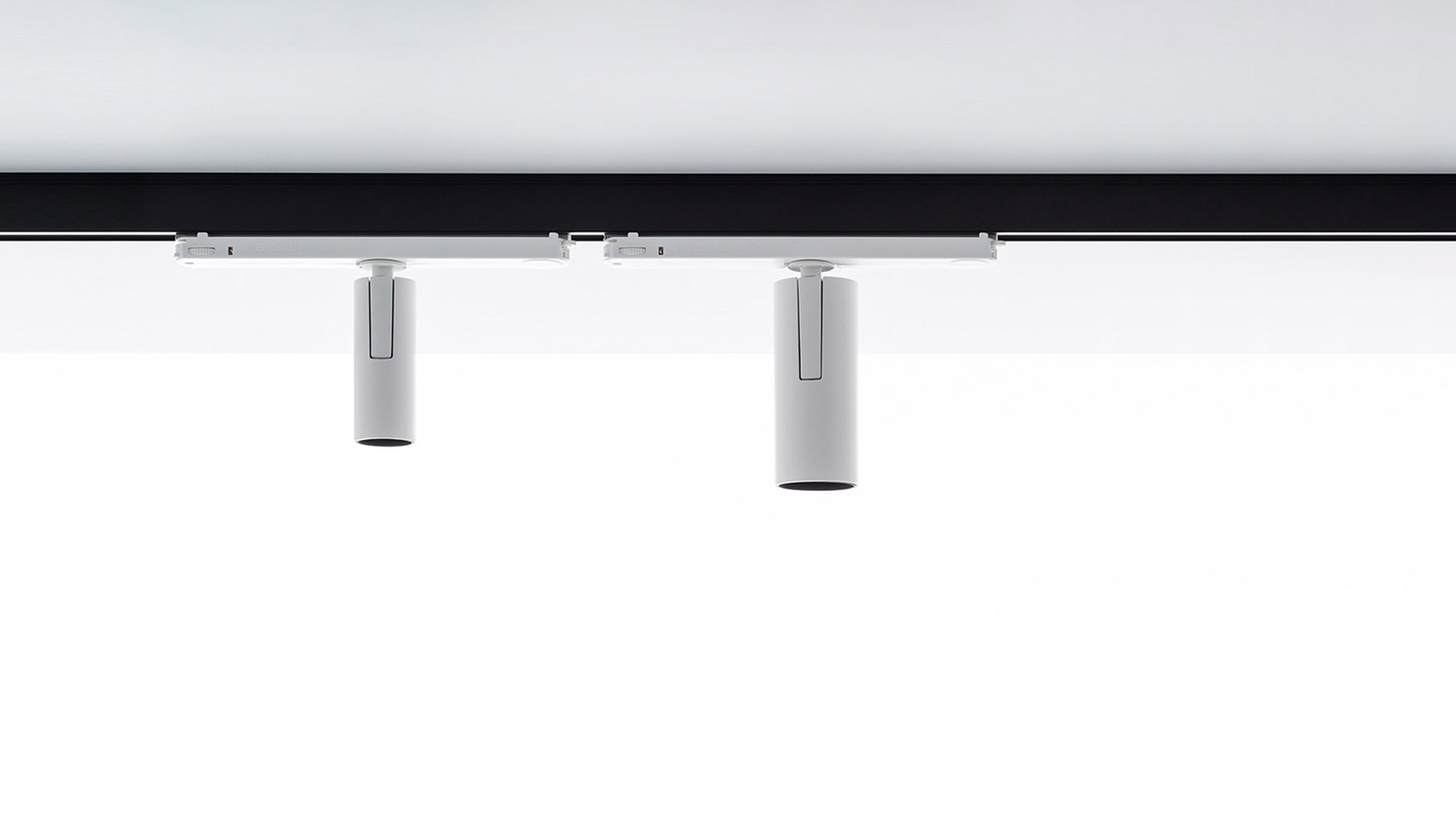 Due faretti cilindrici bianchi Artemide Vector Track 230V montati su binario nero a soffitto, orientati verso il basso.