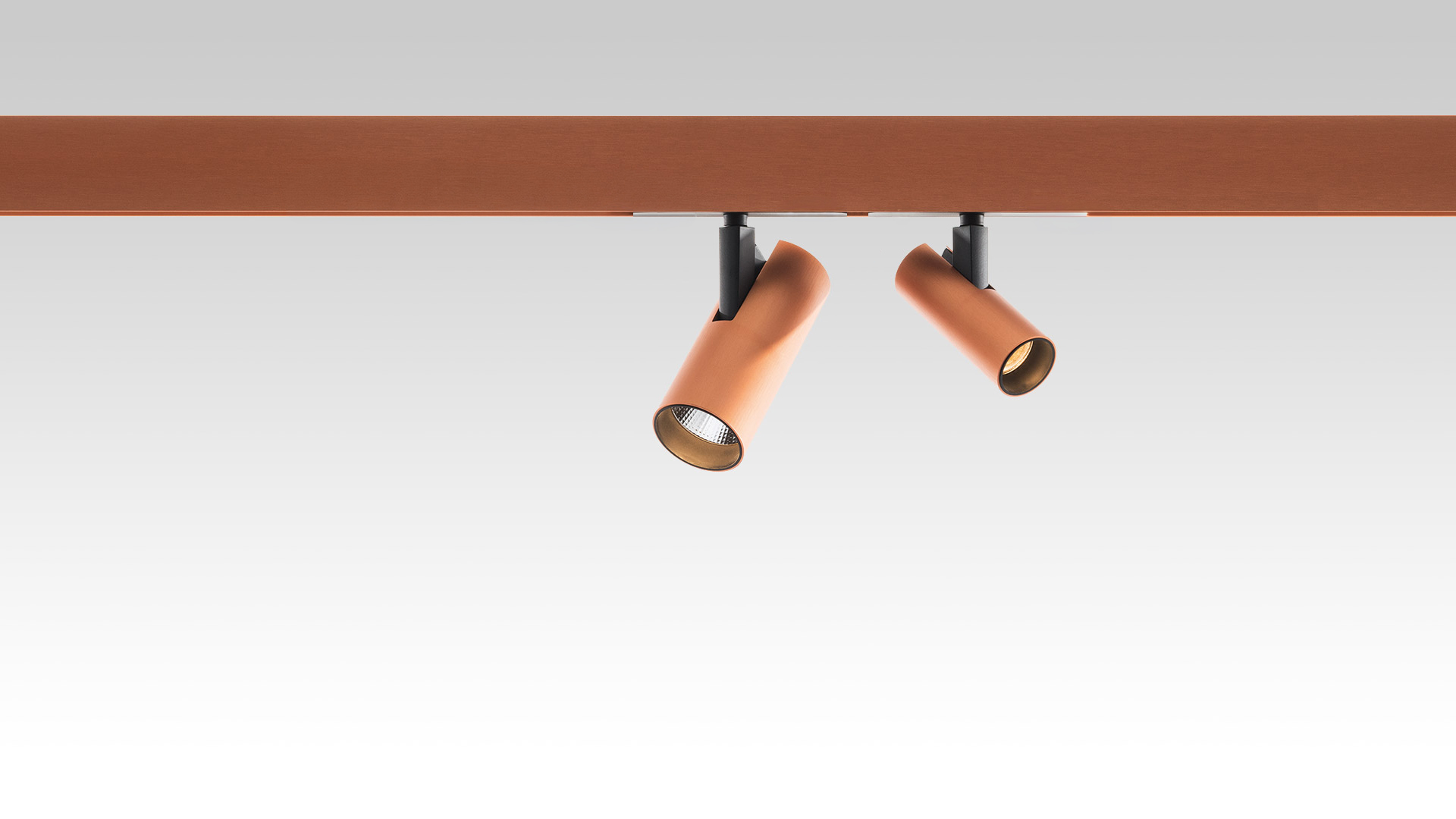 Due faretti LED cilindrici orientabili color terracotta montati su binario magnetico coordinato, inclinati in direzioni diverse