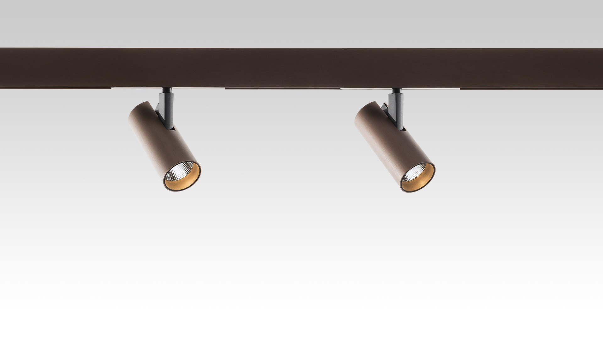 Due faretti cilindrici Artemide Vector Magnetic in bronzo montati su binario magnetico scuro, teste inclinate ad angoli diversi