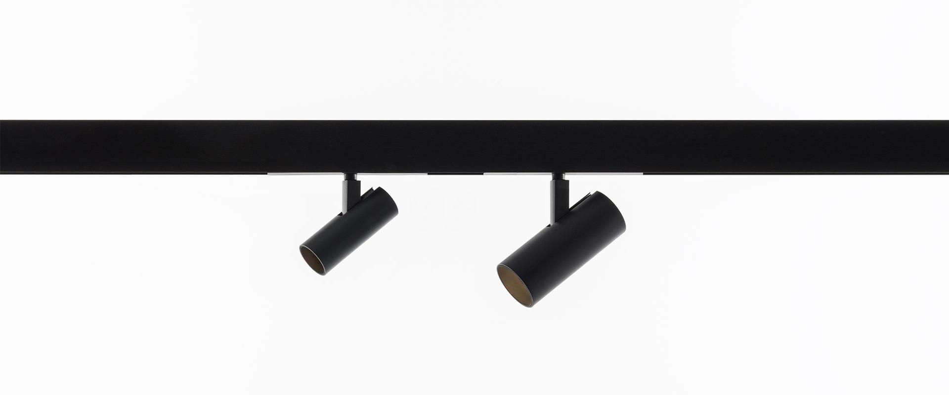 Due faretti cilindrici neri Artemide Vector Magnetic montati su binario nero, orientati in direzioni diverse