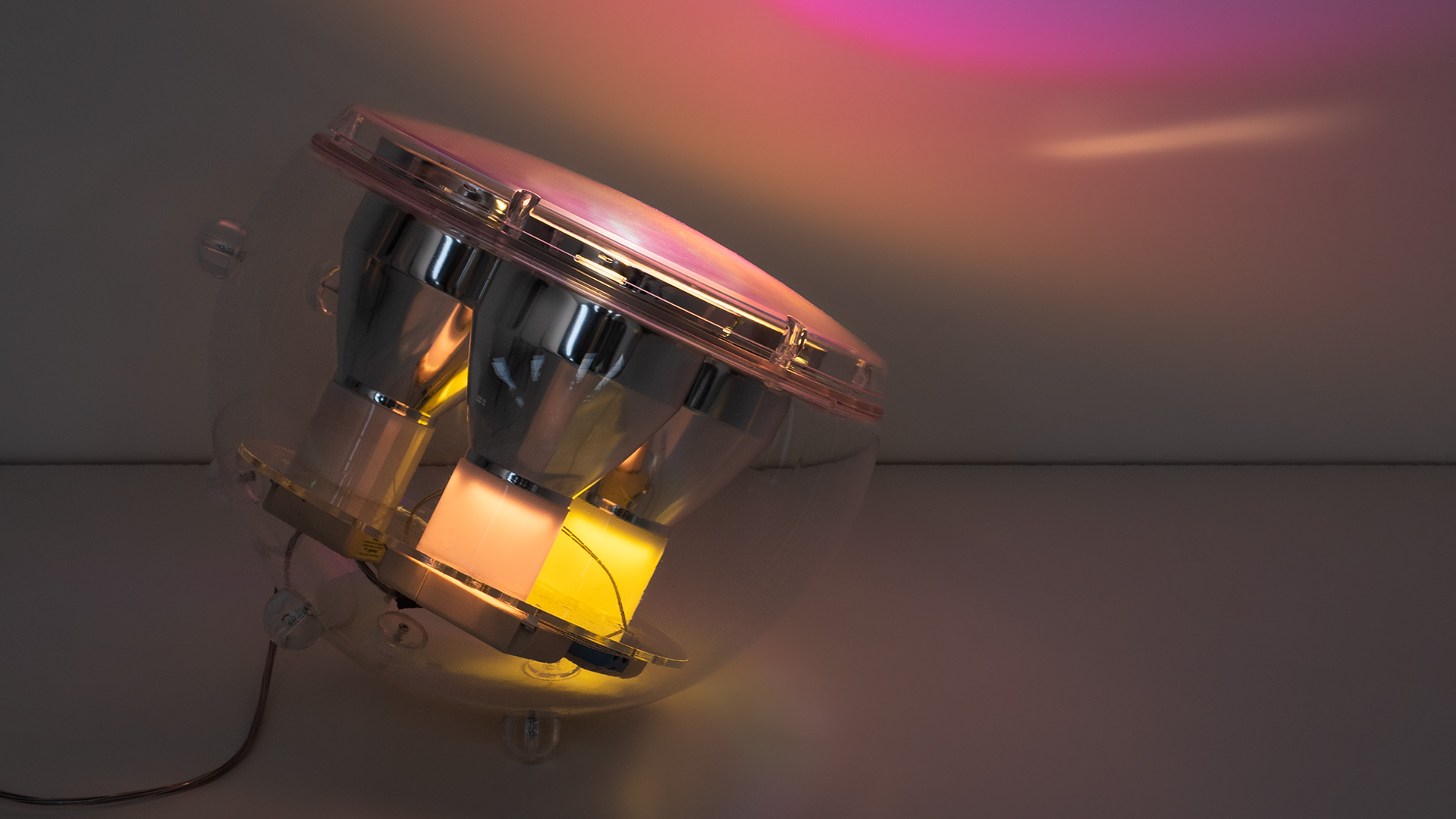 Artemide Yang LED lamp: transparent spherical enclosure with chrome reflectors emitting warm yellow-orange light, casting colorful ambient glow