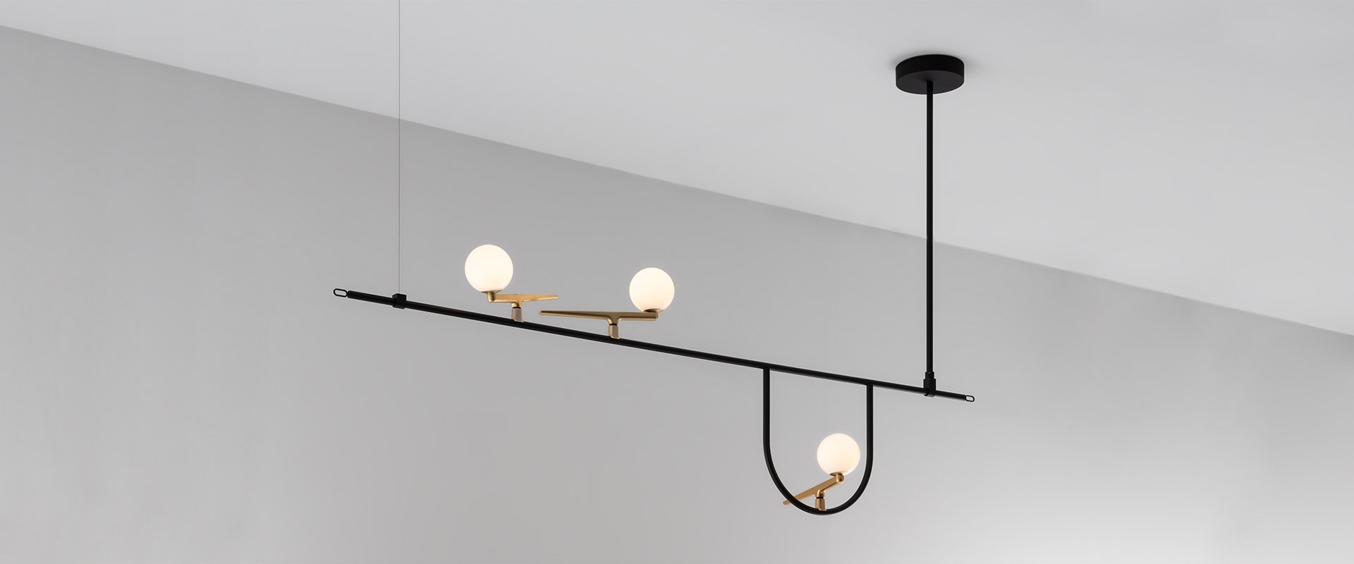 Artemide Yanzi pendant lamp: black horizontal bar with brass accents, three opal glass globe shades at varying heights on black suspension