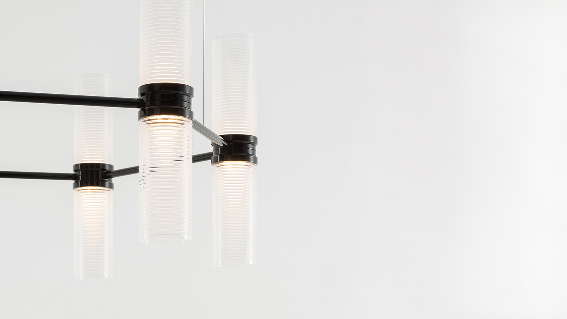 Lampadario Artemide Zephyr con pendenti cilindrici in vetro su più livelli che illumina una cucina moderna con soffitti alti e mobili in legno