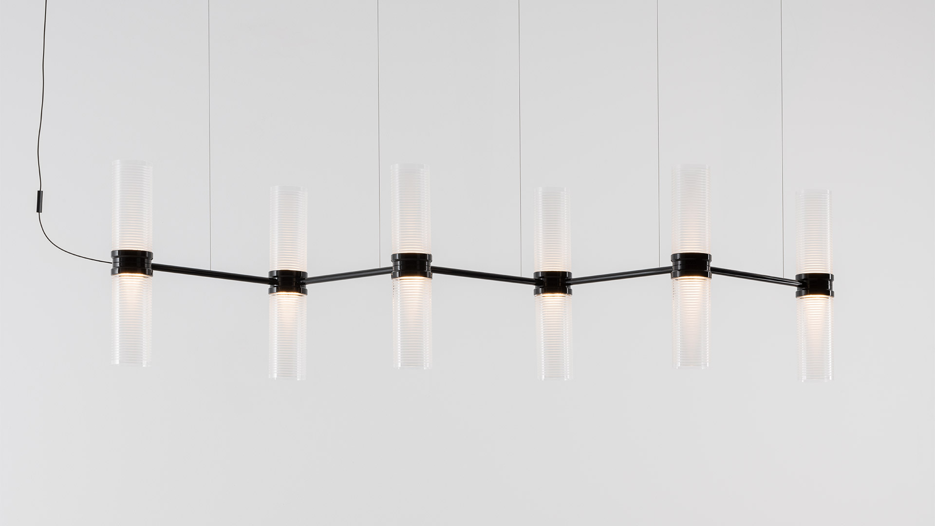 Lampadario a sospensione Artemide Zephyr con sei diffusori cilindrici in vetro costolato su braccio metallico orizzontale, in esterno.